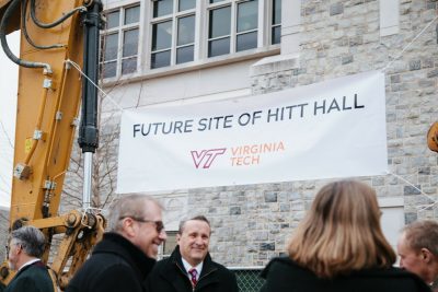 Banner that reads "Future Site of Hitt Hall" held in place by a crane in front of a building.